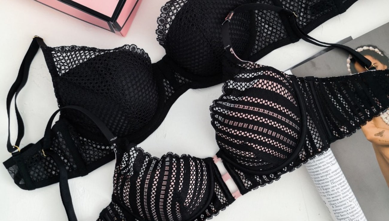 Elegant black bras with mesh designs, one padded, one unpadded, displayed with a pink box.