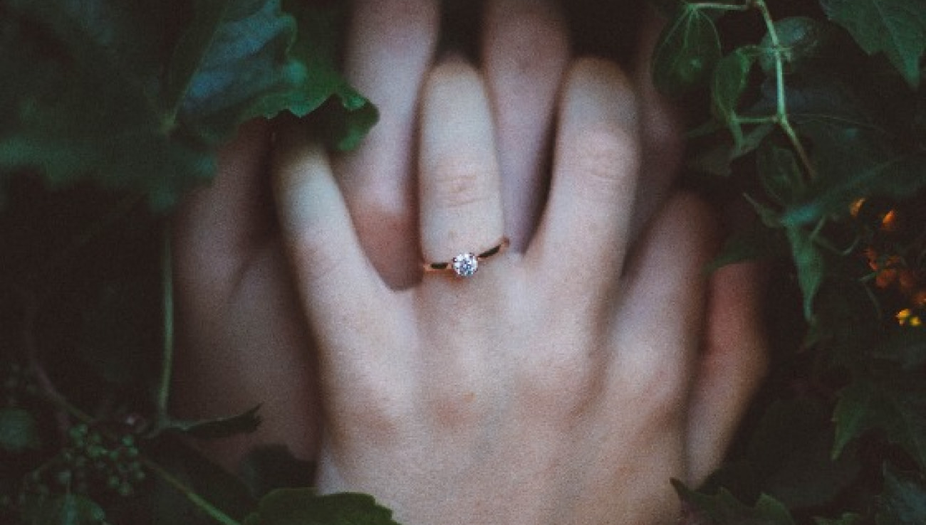 Intertwined hands showcase an elegant engagement ring amidst lush greenery, symbolizing love and commitment.