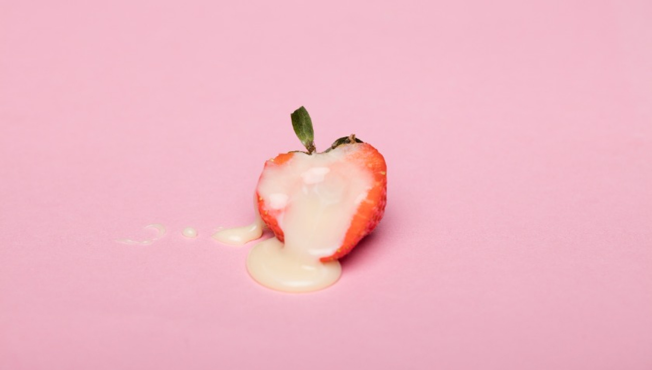 Halved strawberry drizzled with cream against a soft pink background, showcasing freshness and sweetness.