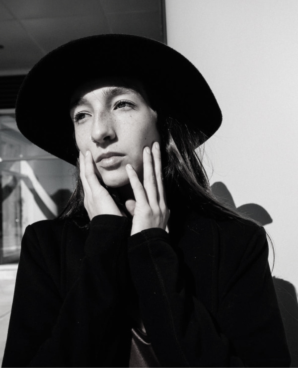 Young person in a black hat, lost in thought against a contrasting urban backdrop.