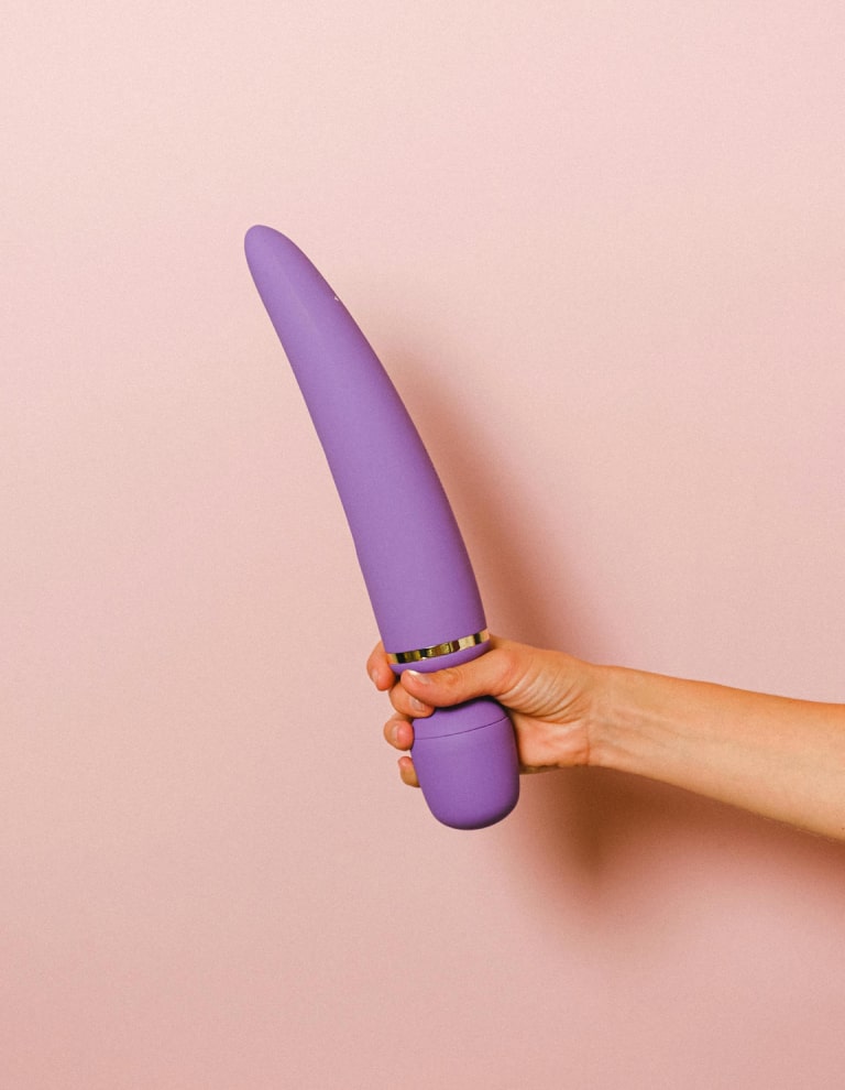 Elegante dispositivo ergonómico morado para el autocuidado, sobre un suave fondo rosa.