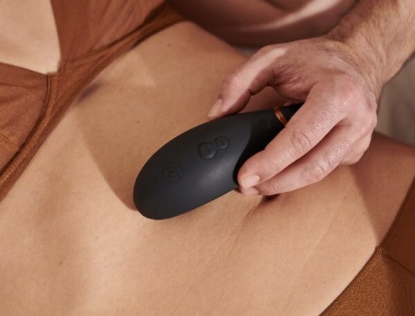 Intimate self-care moment with a person using a black massager in a cozy setting.