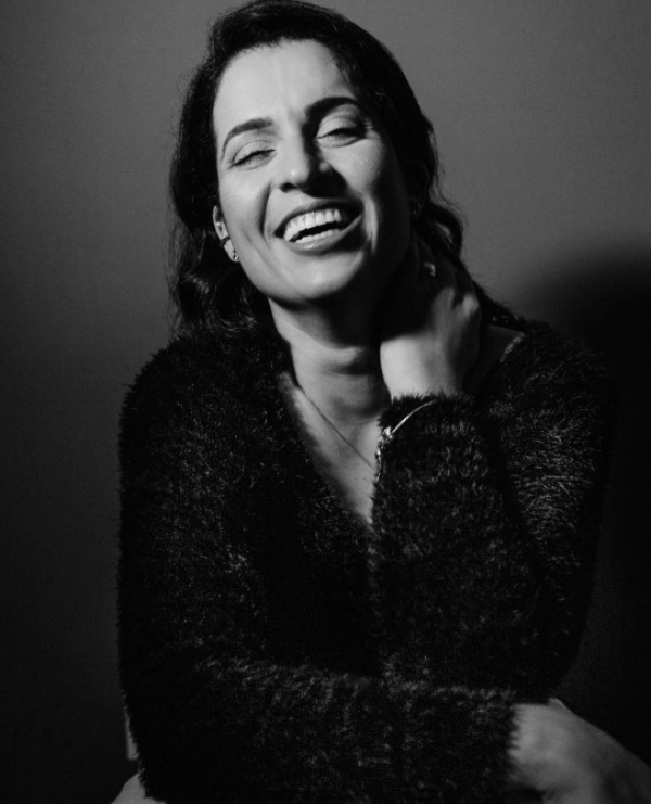 Joyful woman in cozy sweater, radiating warmth in a black-and-white portrait.