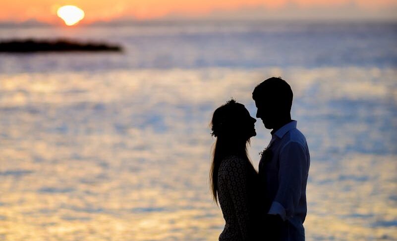 A couple sharing a romantic moment on a beach at sunset, creating a beautiful silhouette.