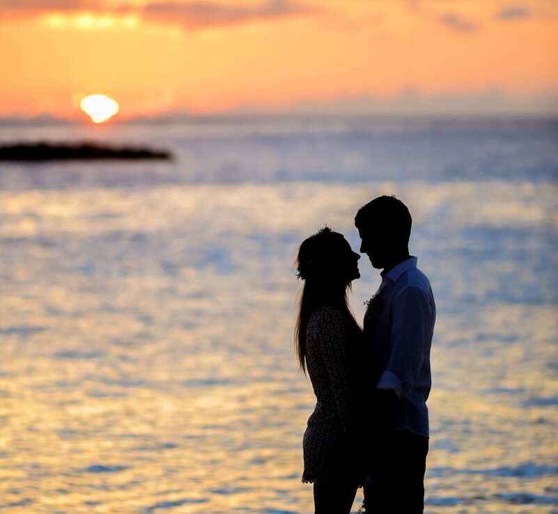 A couple sharing a romantic moment on a beach at sunset, creating a beautiful silhouette.