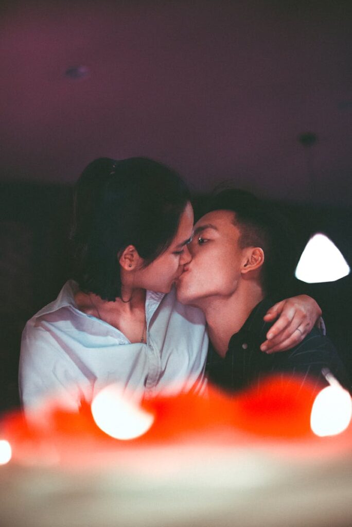 A romantic kiss shared by an Asian couple, captured in a warm, intimate setting.