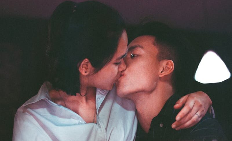 A romantic kiss shared by an Asian couple, captured in a warm, intimate setting.