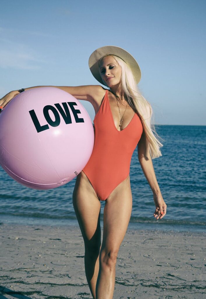 Young woman in swimsuit holding a pink love ball on Miami beach.