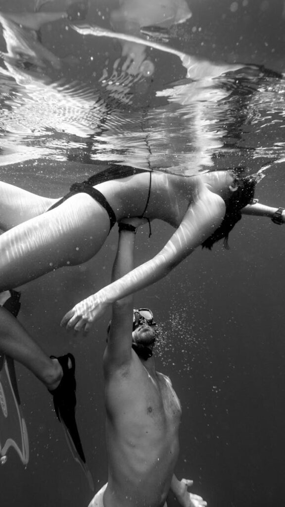 A man and woman snorkeling underwater in a black and white photograph.