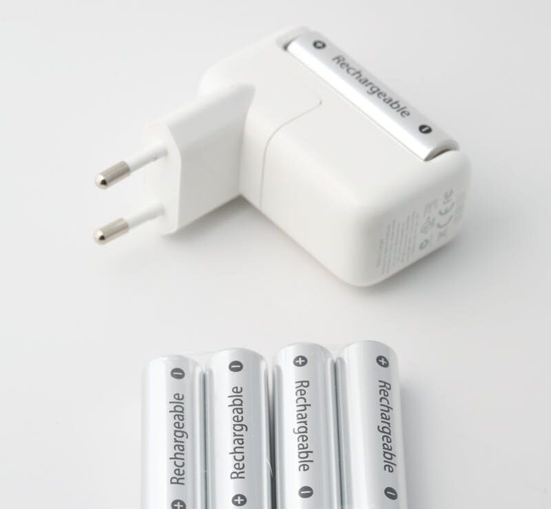 Gros plan d'un chargeur de batterie et de piles rechargeables sur fond blanc, idéal pour les thèmes de la technologie et de l'énergie.