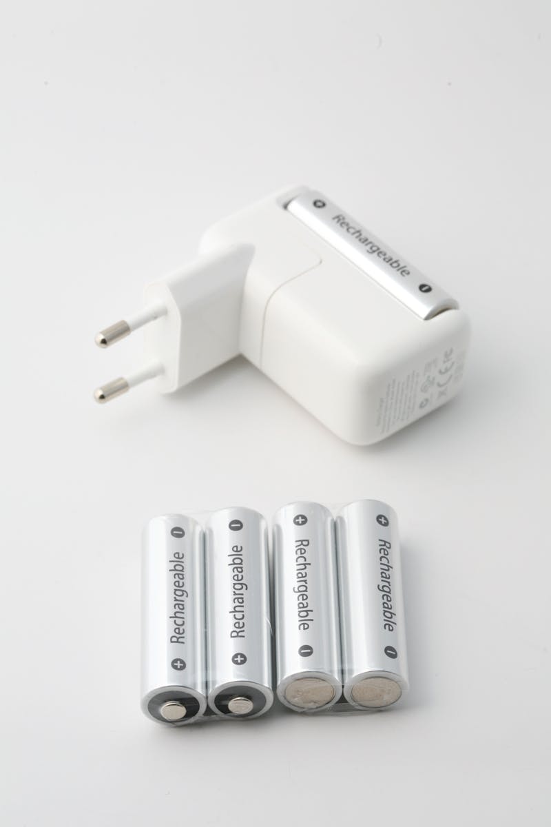 Primo piano di un caricabatterie e di batterie ricaricabili su sfondo bianco, perfetto per temi tecnologici ed energetici.