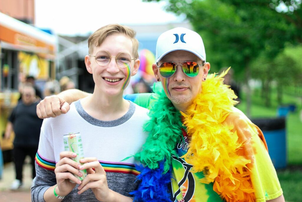 Duas pessoas a sorrir e a abraçarem-se num vibrante festival de orgulho ao ar livre com as cores do arco-íris.