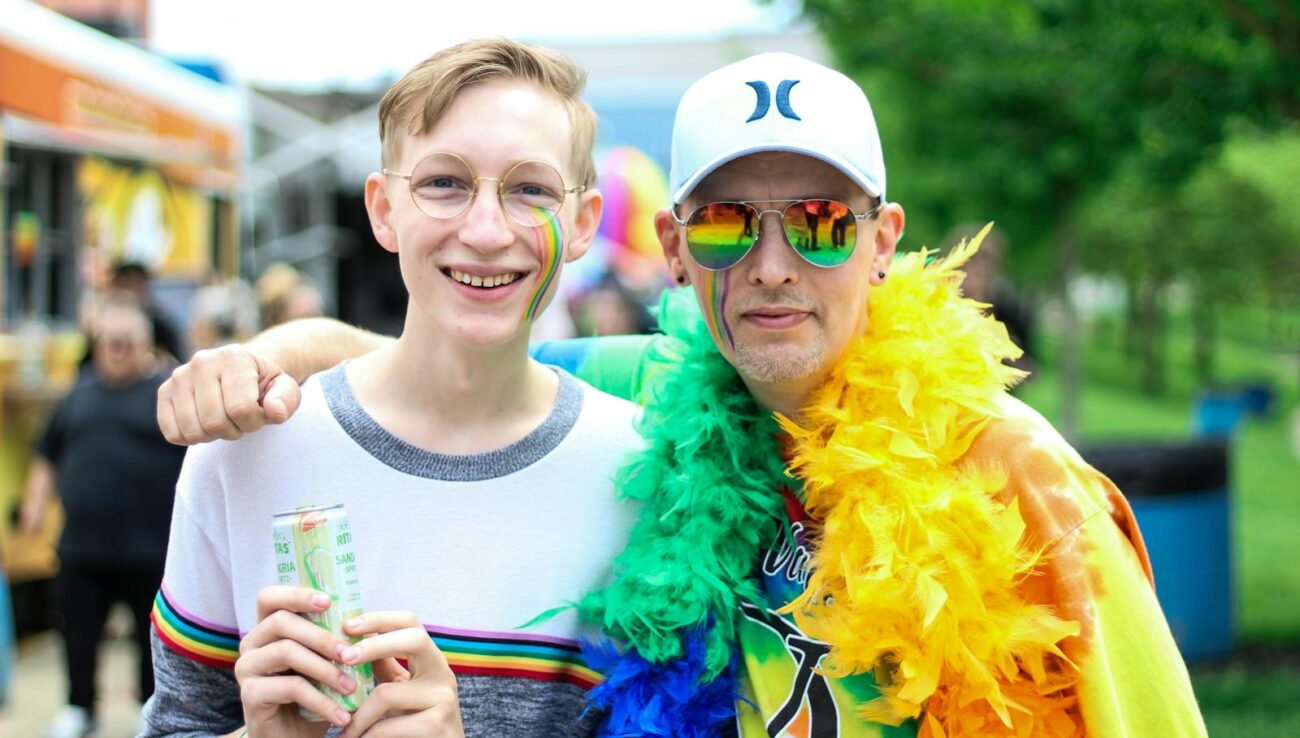 Dos personas sonríen y se abrazan en un vibrante festival del orgullo al aire libre con los colores del arco iris.