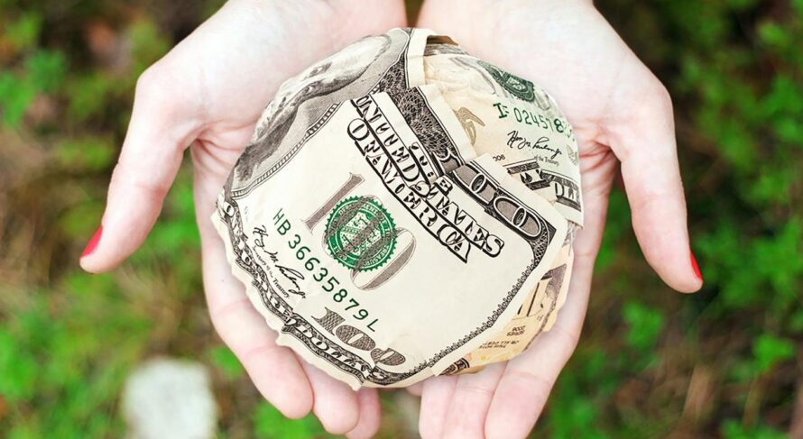 Hands holding crumpled money outdoors, symbolizing charity and financial support.