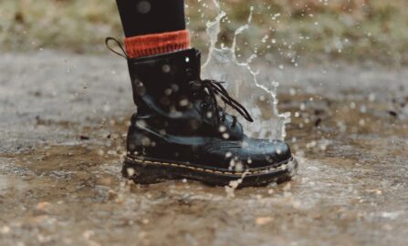 Крупный план водонепроницаемых ботинок, которые плещутся в луже в дождливый день на улице.