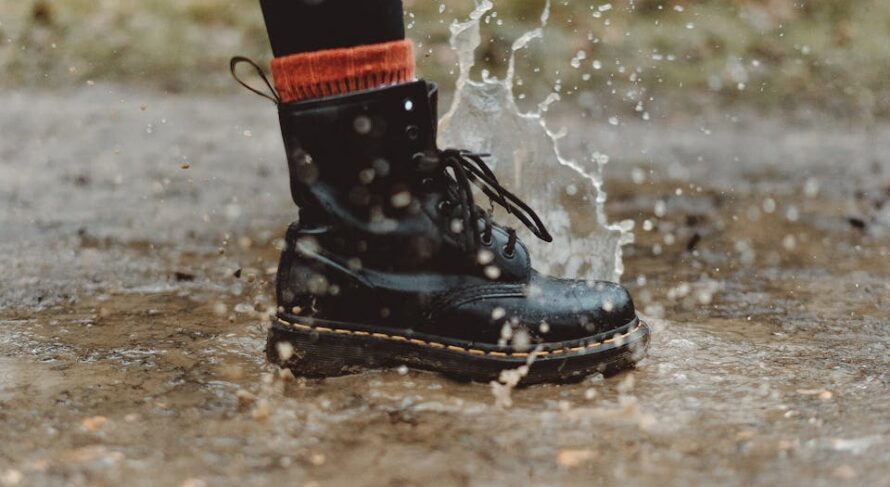 Close-up of waterproof boots splashing through a puddle on a rainy day outdoors.