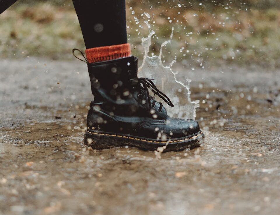 Close-up of waterproof boots splashing through a puddle on a rainy day outdoors.