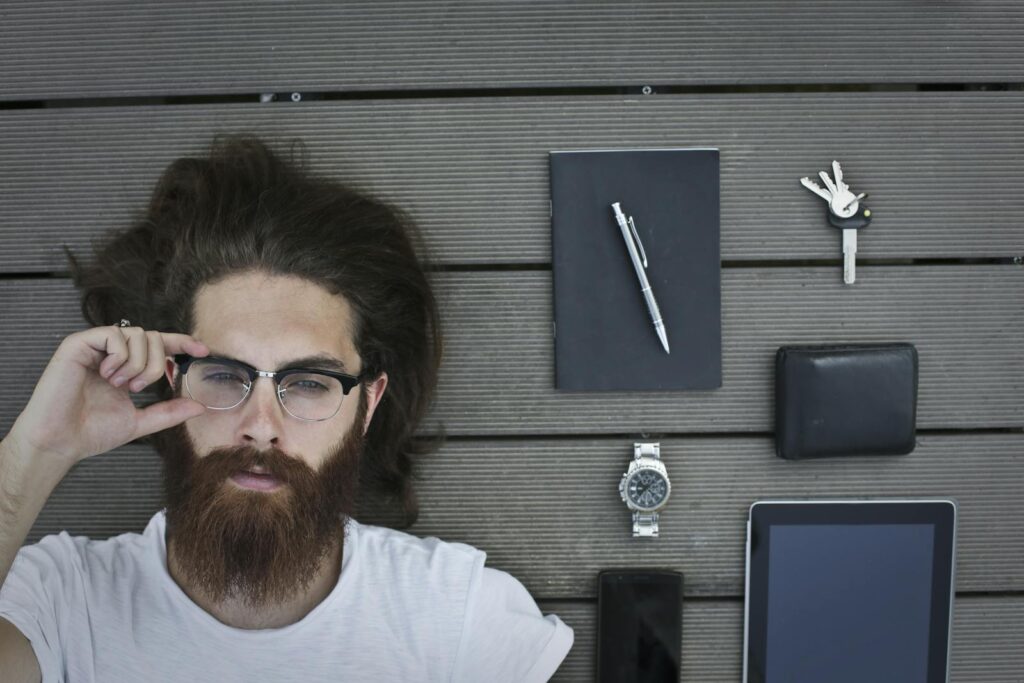 Ritratto di un uomo barbuto sdraiato su una terrazza in legno con gadget e accessori.