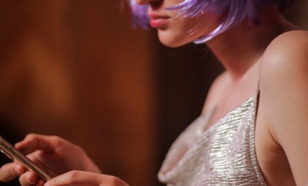 元気なスタイルデジタル接続に熱中する若者たち 室内でスマートフォンを使用するバイオレットのかつらときらびやかなドレスの若い女性。