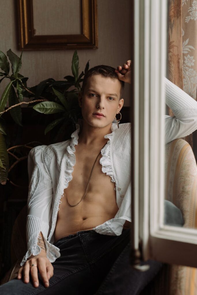 Shirtless man in elegant attire sitting by the window with natural light.