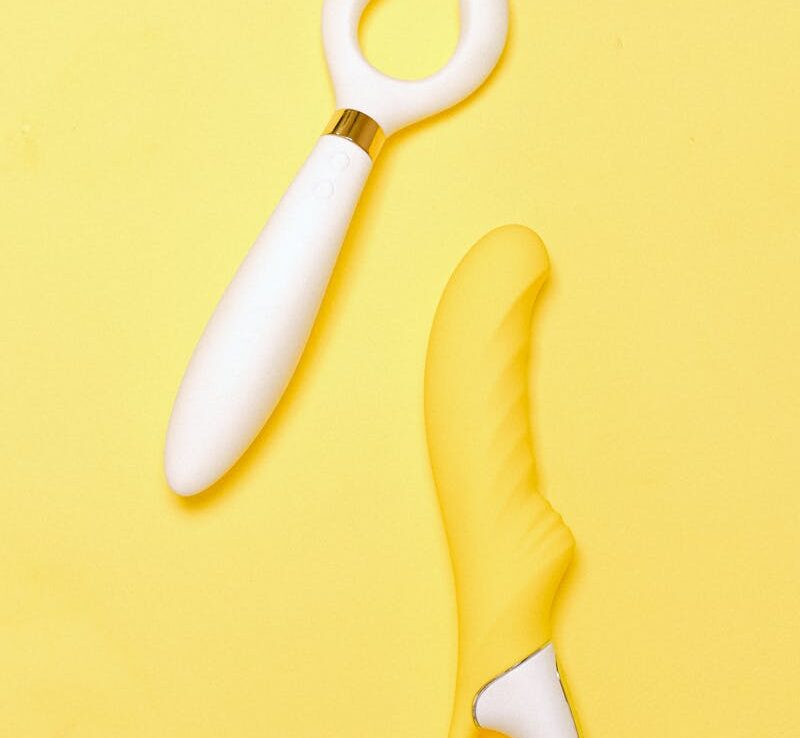 Bright flat lay of silicone sex toys on vibrant yellow backdrop.