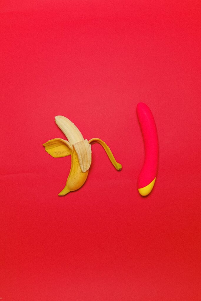 Une banane pelée et un vibromasseur rose sur un fond rouge vibrant symbolisant la sexualité.