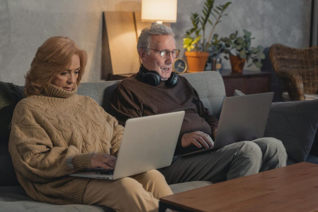 Senior couple using laptops on the sofa for online activities and work.