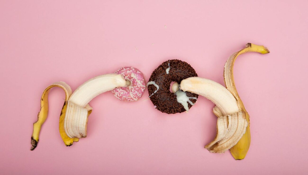 Bananer og donuts: En legende lækkerbisken Legende arrangement af skrællede bananer og donuts på en lyserød baggrund, perfekt til konceptuel kunst.