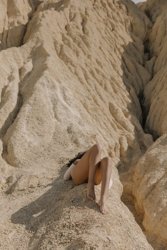 A woman lies barefoot on a sandy hill, capturing a serene summer moment.