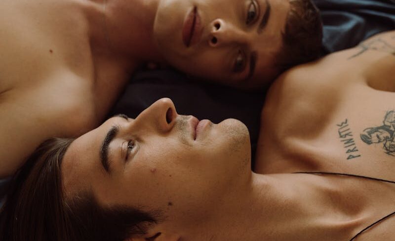 A tender and intimate portrait of two shirtless men lying together indoors, expressing love and connection.