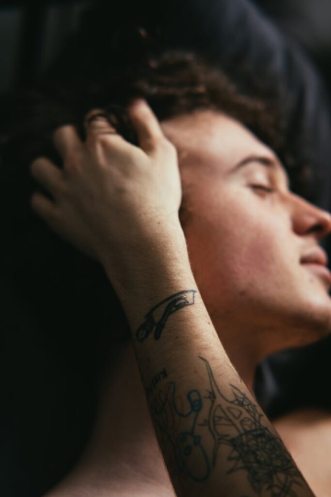 Close-up of a young man relaxing indoors, highlighting tattoos on his arm with a calm mood.