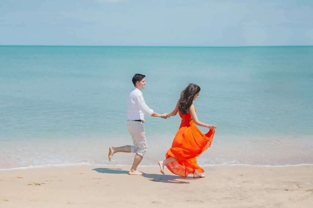 A joyful couple runs barefoot along Baku's sunny coastline, embodying carefree summer love.