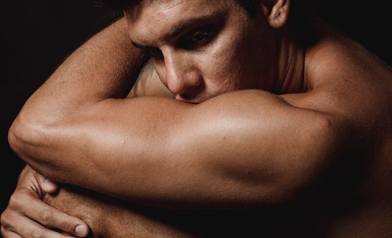 Dramatic portrait of a shirtless man sitting, deep in thought, in a studio setting.