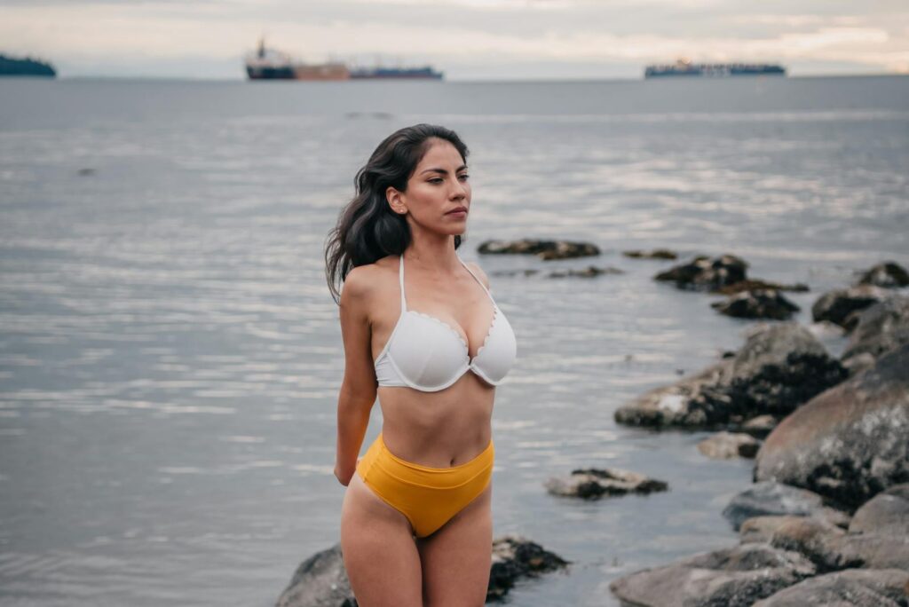 Femme en maillot de bain au bord d'un océan rocheux, dégageant force et sérénité.