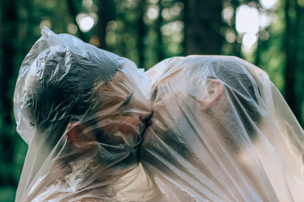 A couple embracing and kissing under a plastic cover in a forest setting.