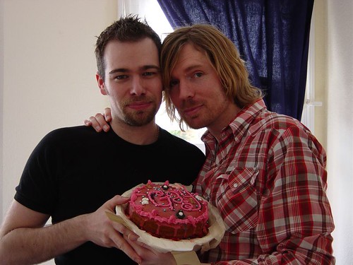 Two friends joyfully celebrate with a vibrant cake, sharing laughter and warmth in a cozy indoor setting.