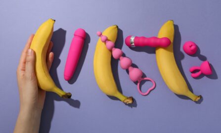 Бананы и игривые розовые предметы удовольствия на фиолетовом фоне Коллекция секс-игрушек на фиолетовом фоне.