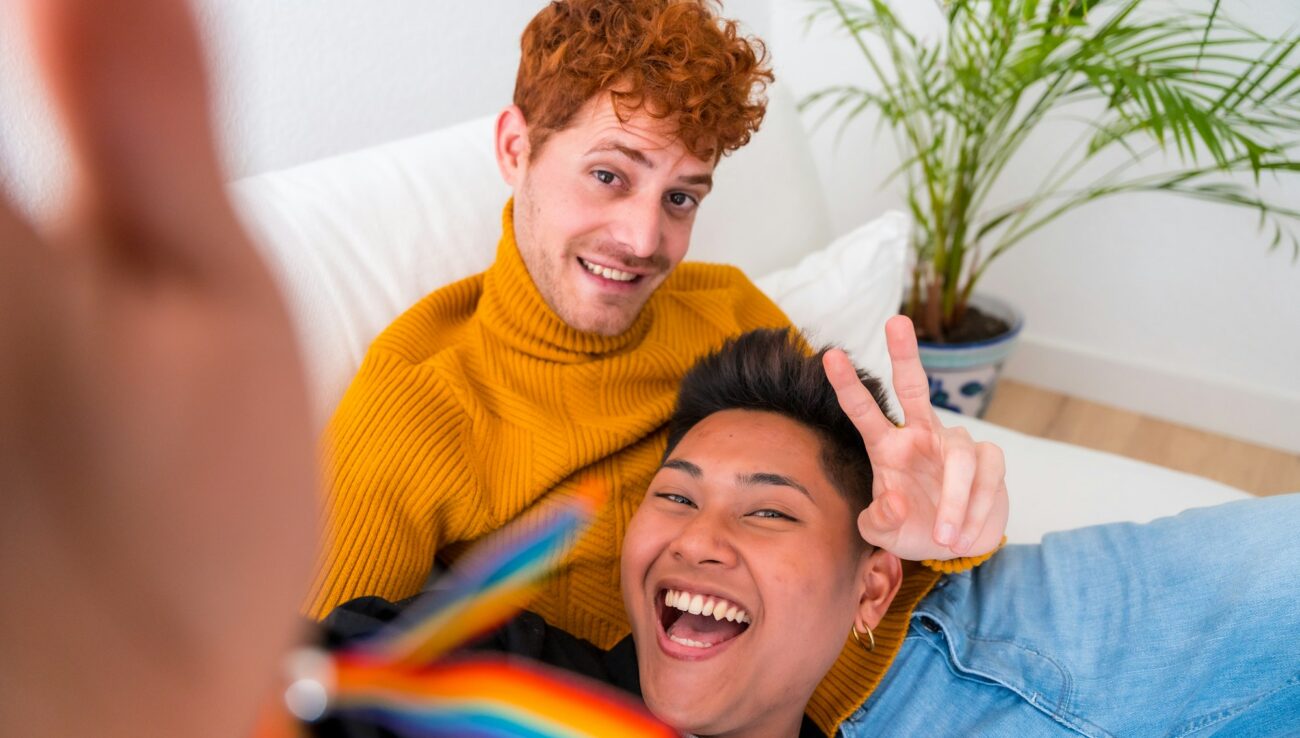 Beautiful gay couple being romantic indoors at home on the sofa, gay couple taking selfie and making