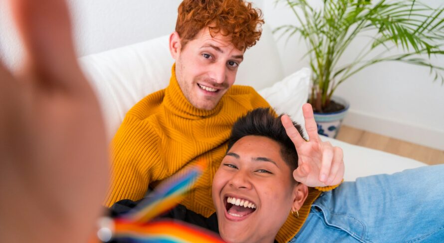 Beautiful gay couple being romantic indoors at home on the sofa, gay couple taking selfie and making