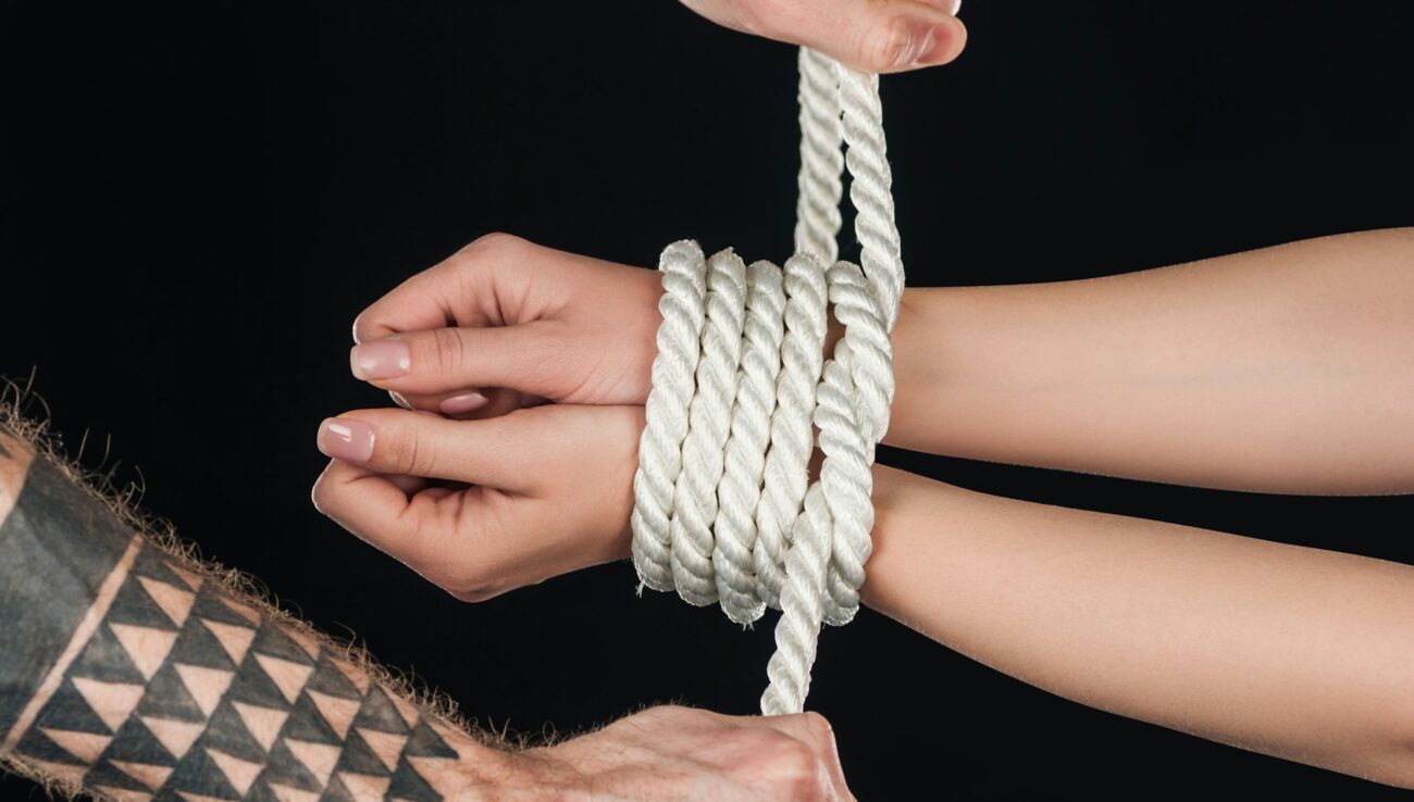 close up of tattooed man tying rope on female hands isolated on black