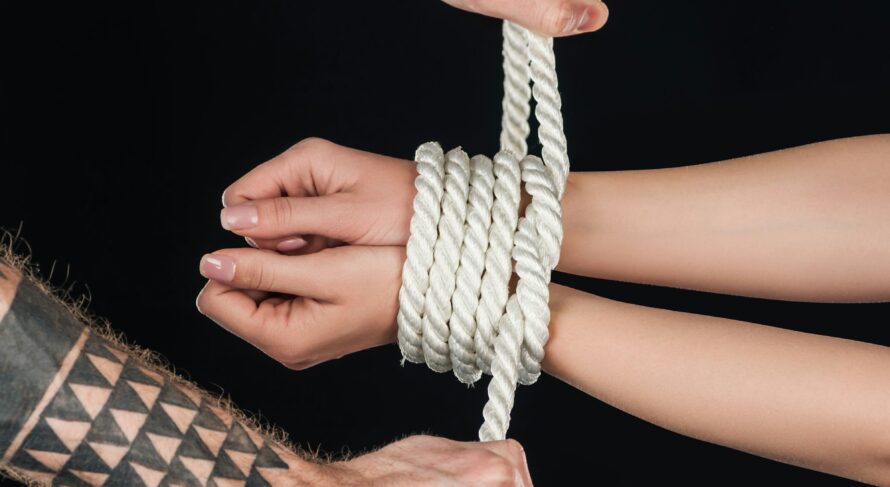 close up of tattooed man tying rope on female hands isolated on black