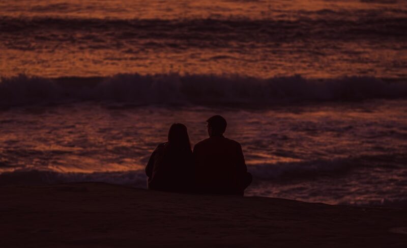 a couple of people sitting on top of a sandy beach