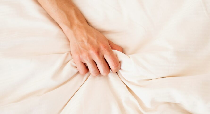 Female hand grasping on white bed, sign of woman orgasm