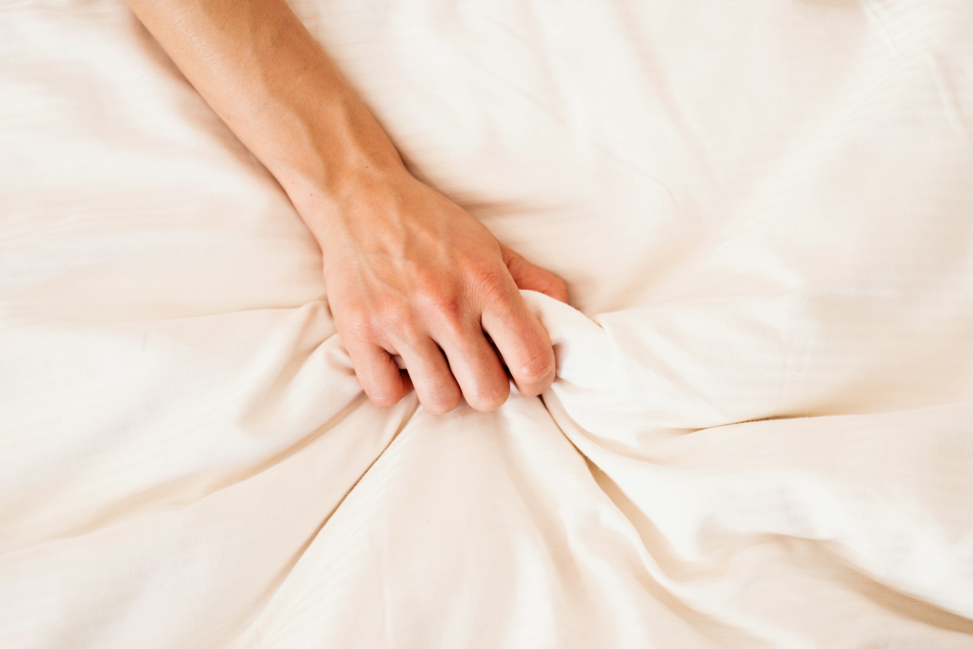 Mano femminile che si afferra sul letto bianco, segno di un orgasmo femminile