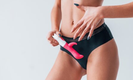 Jente i svart undertøy som står med rosa sexleketøy i hendene i studioet. Forestilling om intimitet