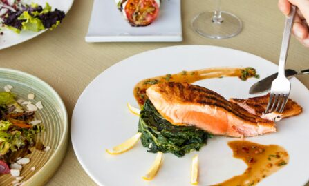 Elegant laxrätt med färska grönsaker och vin tillagad fisk på vit keramiktallrik