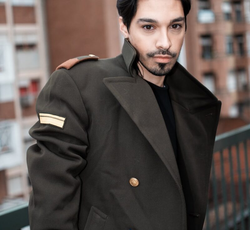 um homem de cabelo preto e barba, vestindo um casaco