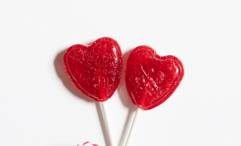 two heart shaped lollipops tied up on a white surface