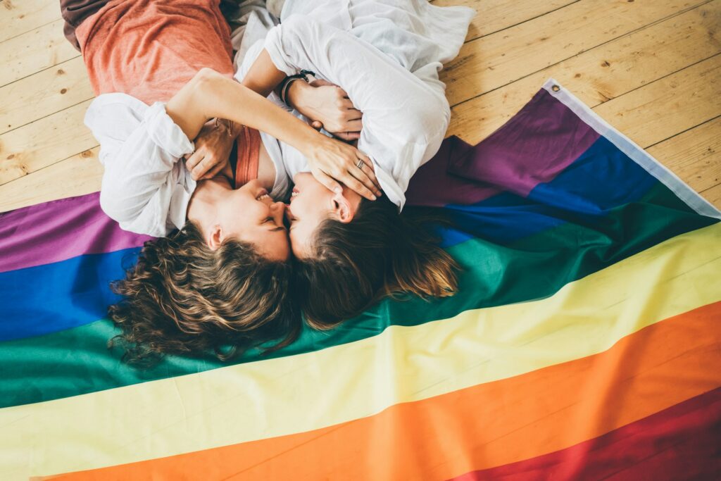 Couple de lesbiennes amoureuses, allongées et se serrant dans le drapeau arc-en-ciel.