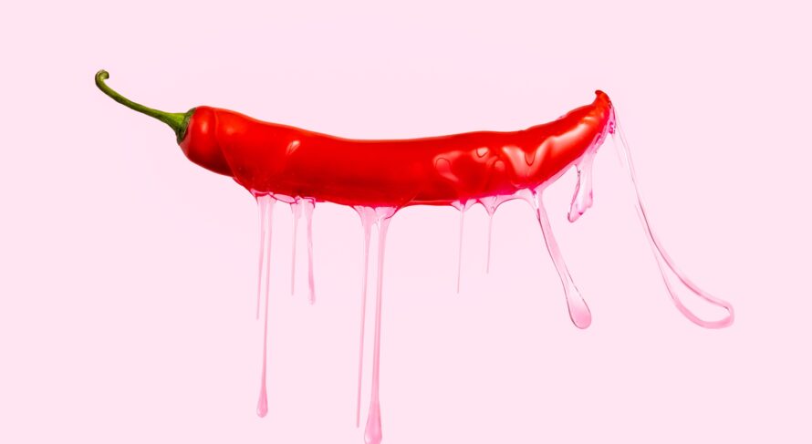 Red chili pepper with dripping pink gel on pink background.